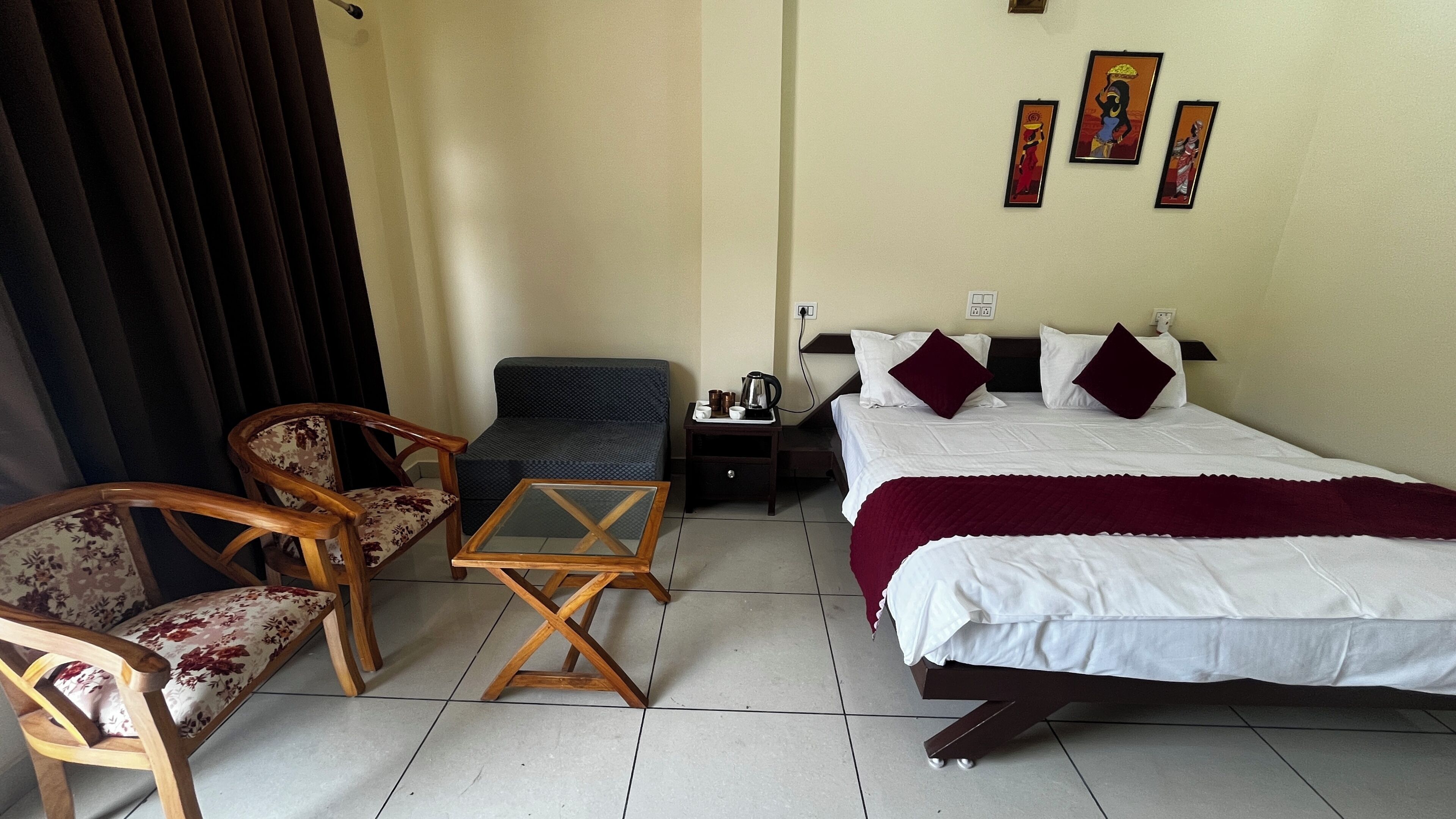 Une chambre d’hôtel comprenant un lit, deux chaises, une petite table, une table de chevet et un mur orné de trois tableaux encadrés.