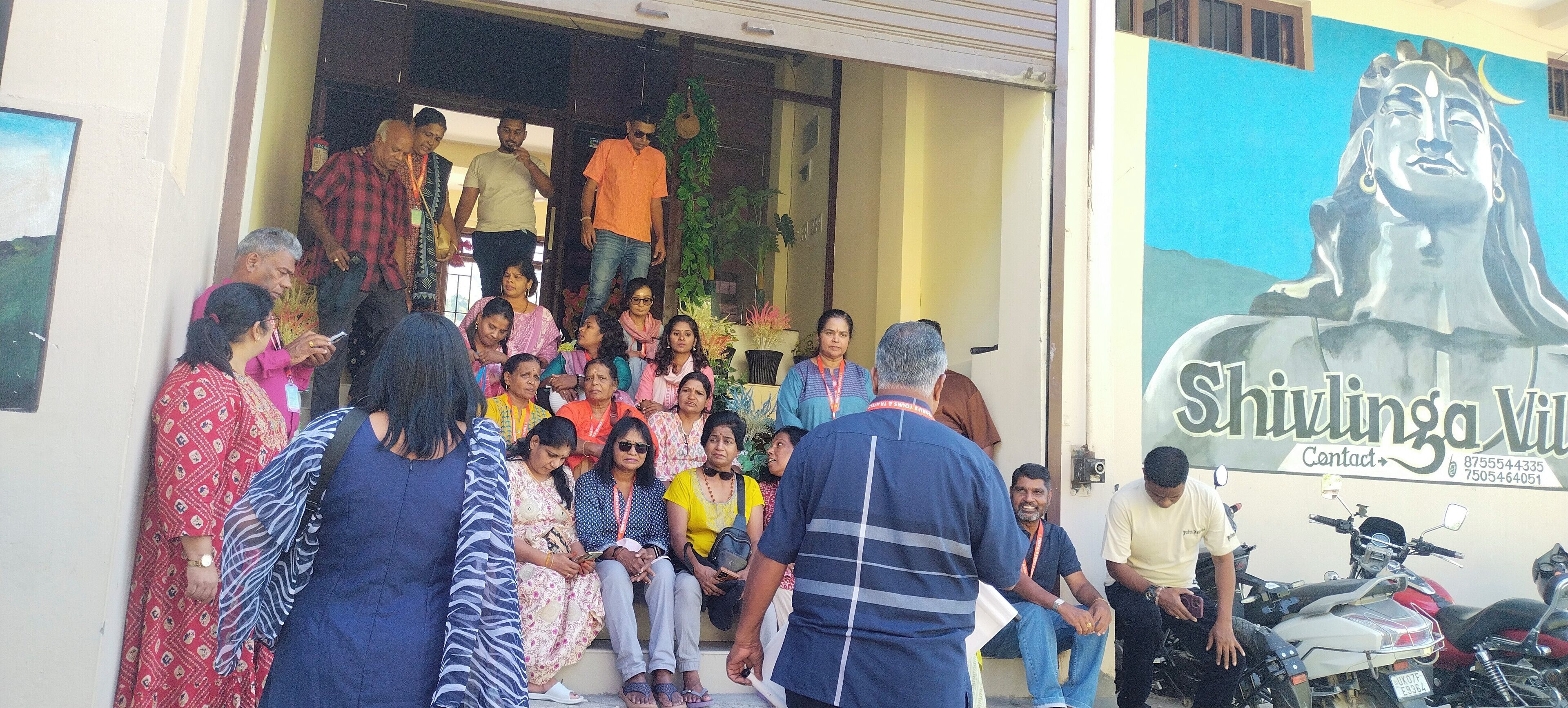 A group of people exiting a building with a sign reading "Shivlinga Villa Contact".