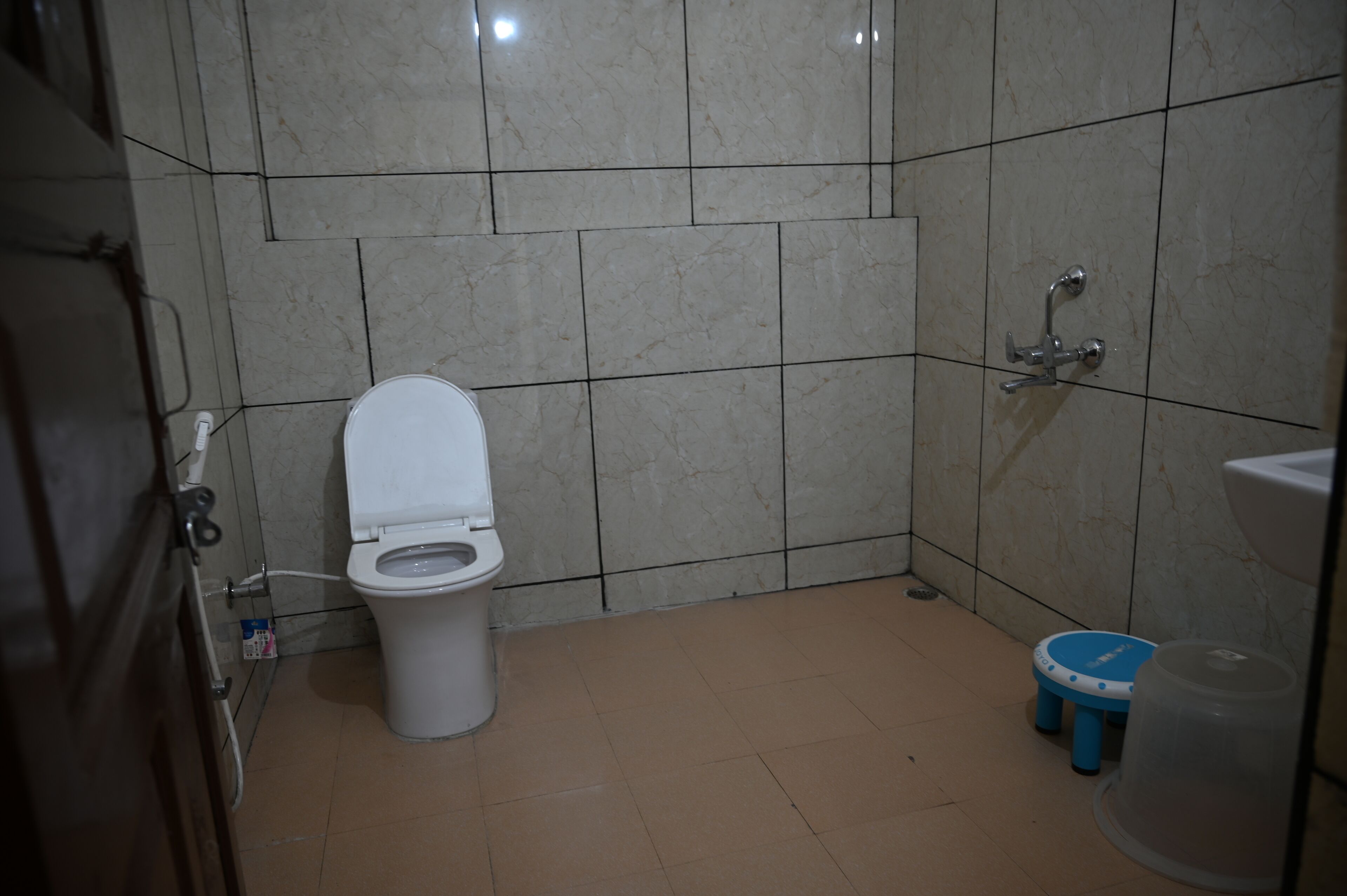Une salle de bain avec des toilettes, une douche et un petit tabouret bleu.
