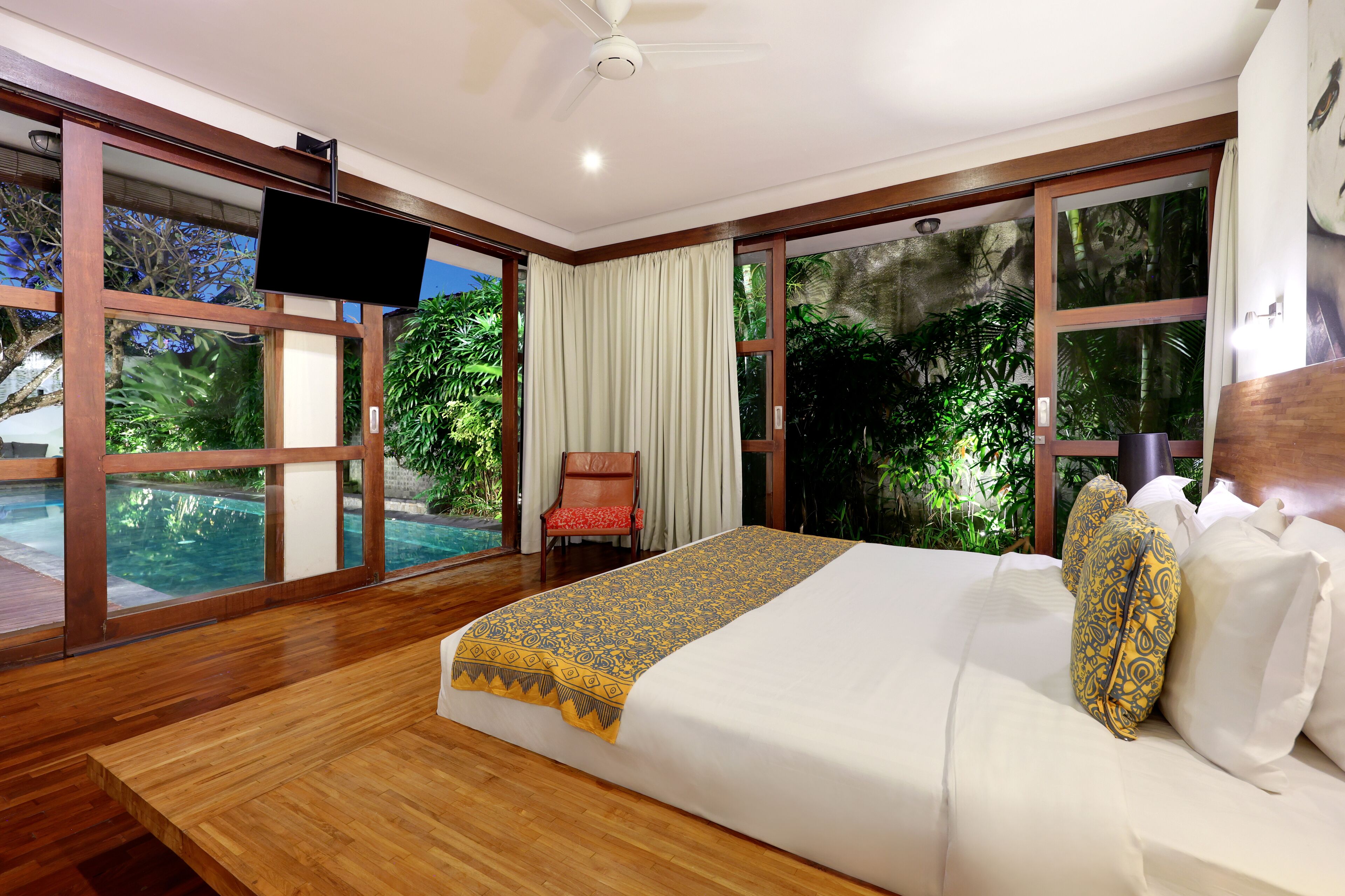 A spacious bedroom with a large bed, a flat-screen TV, and a view of a swimming pool.