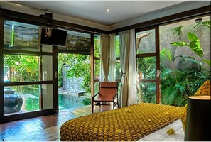 Un dormitorio con un ventanal grande, una cama, una silla y un televisor.