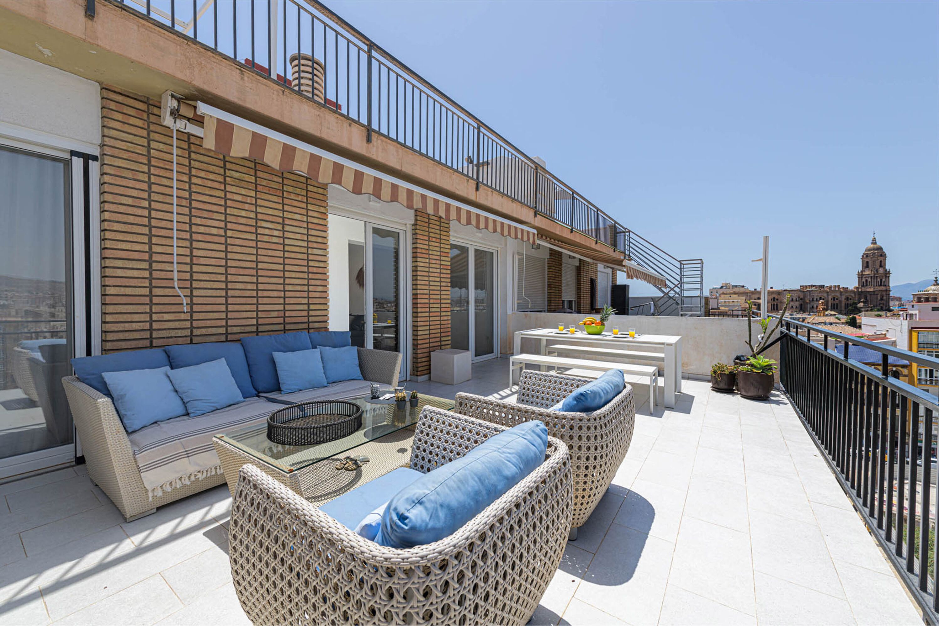 A rooftop terrace with wicker furniture, a dining area, and a view of a historic building in the background.