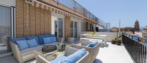 A rooftop terrace with wicker furniture, a dining area, and a view of a historic building in the background.