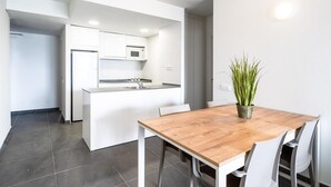 A modern kitchen with white cabinetry, a wooden dining table, and a potted plant. - Chic Stay by the Beach (Tarragona)