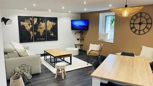 Una sala de estar moderna con un sofá, una mesa de centro y un televisor. Hay estantes montados en la pared y un reloj grande.