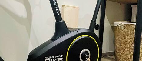 A compact bike exercise machine in a room with a tiled floor, a wooden cabinet, and a wicker basket.