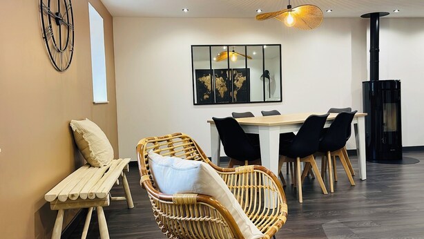 Un comedor moderno con una mesa y sillas de madera, una silla de mimbre, un banco y un reloj en la pared.