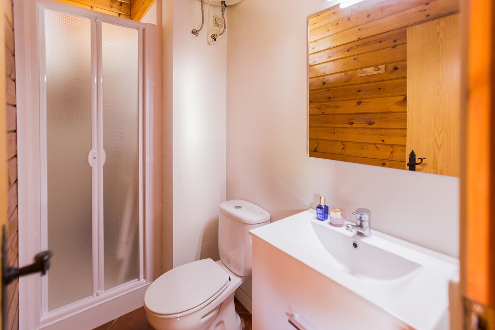 Casa de banho com chuveiro em cabine de vidro, sanita branca e lavatório branco com espelho em cima.