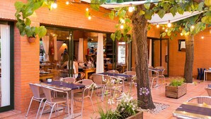 Un espace extérieur aménagé en terrasse, avec des murs en briques, des tables, des chaises et des guirlandes lumineuses.