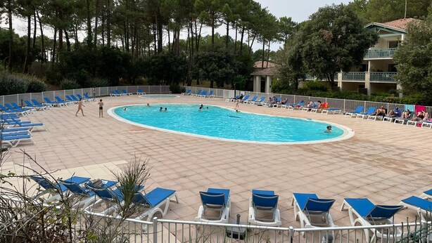 A swimming pool with blue lounge chairs and a building in the background.