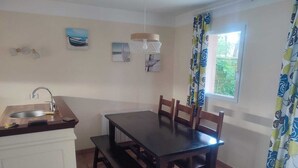 A compact kitchen with a sink, wooden table, and chairs, a window with curtains, and wall art.