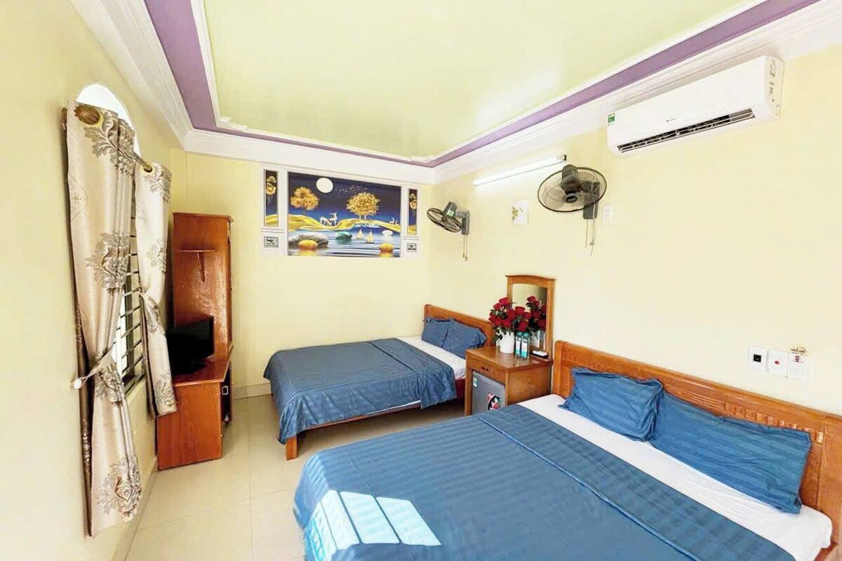 Habitación de hotel con dos camas, un armario de madera, ventilador de techo, aire acondicionado y un cuadro en la pared.
