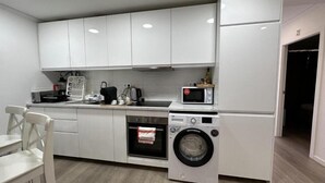 Una cocina compacta con armarios blancos, microondas, lavadora y un lavamanos pequeño.