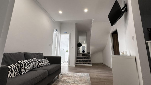 Una sala de estar moderna con un sofá gris, almohadones a rayas negras y blancas, piso de madera y una escalera que conduce a otra habitación.