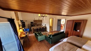 A room with a bed, a desk, a chair, a kitchenette, and a door leading to another room.