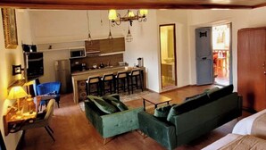 A cozy living room with a green sofa, a dining area with a bar, and a kitchen in the background.