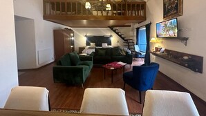 A spacious living area with a high ceiling, a wooden balcony, a television, and a staircase leading to an upper level.