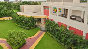 A modern building with a curved entrance, outdoor seating, and lush greenery. - Sinclairs Burdwan (Burdwan)