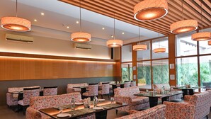 A restaurant with floral-patterned chairs and tables, large windows, and hanging pendant lights. - Sinclairs Burdwan (Burdwan)