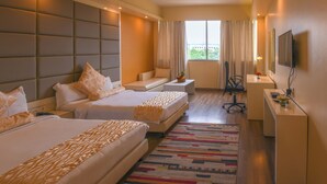 A hotel room with two beds, a desk, a chair, a TV, and a window with curtains. - Sinclairs Burdwan (Burdwan)