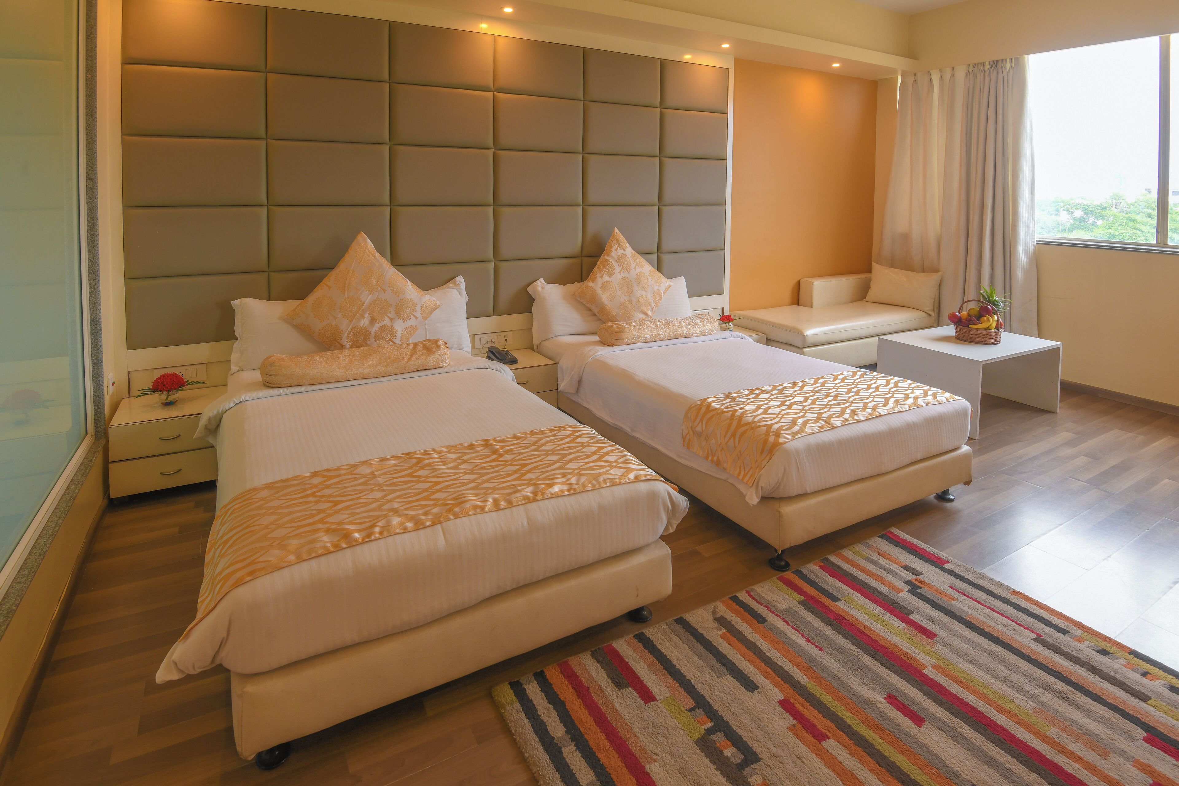 A hotel room with two beds, a sofa, a small table, and a large window.