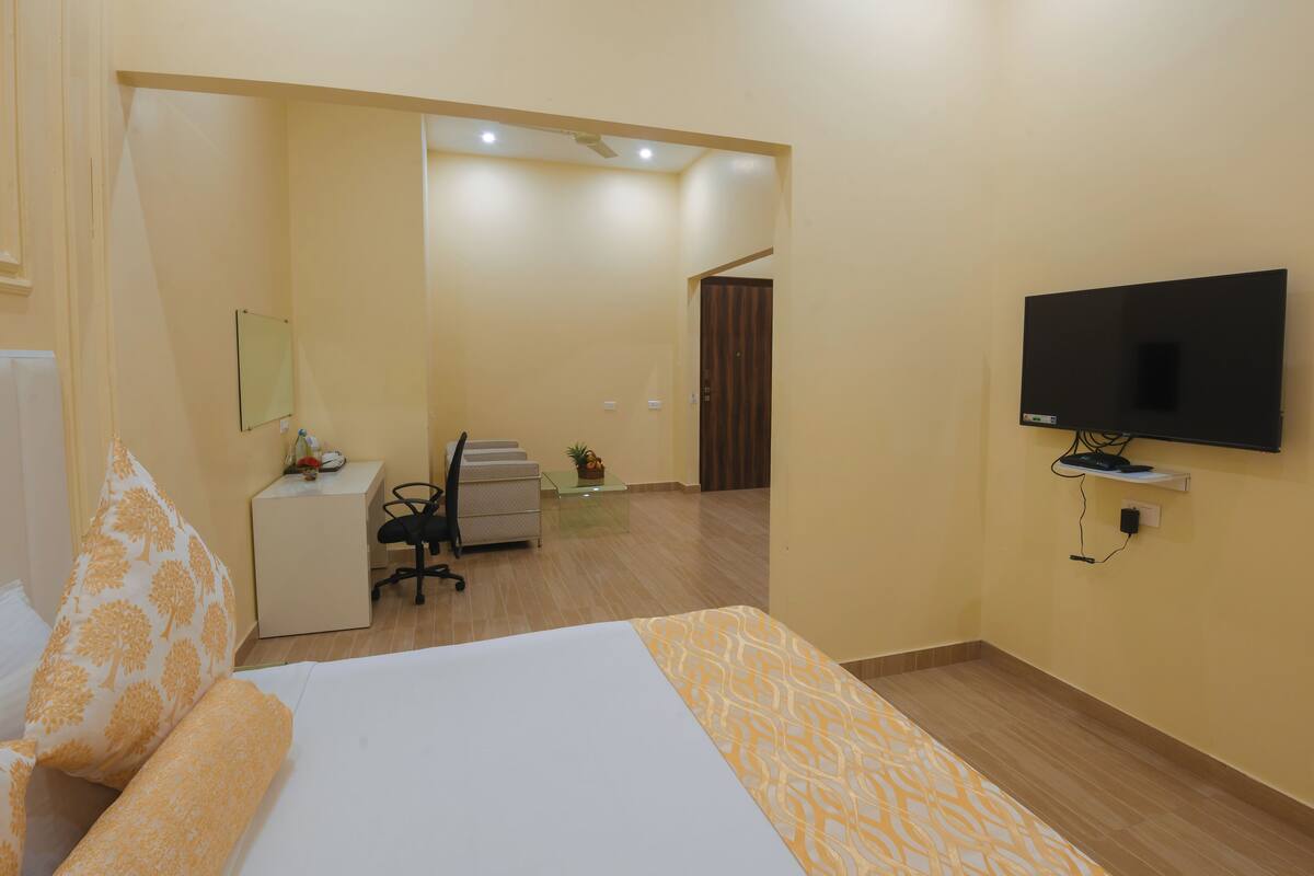 Una habitación de hotel con cama, escritorio, silla, televisión y una puerta que da a otra habitación.