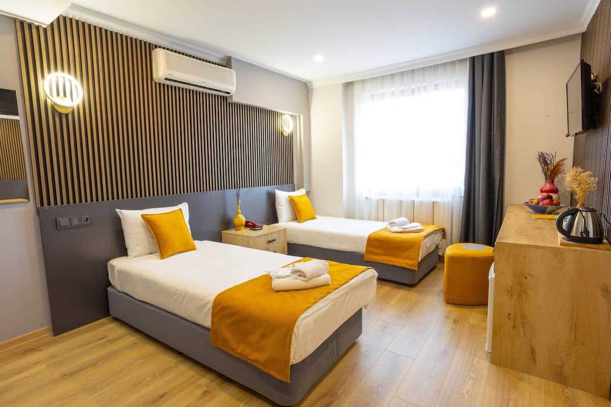 A hotel room with two beds, a wooden headboard, a wooden desk, and a large window with curtains.