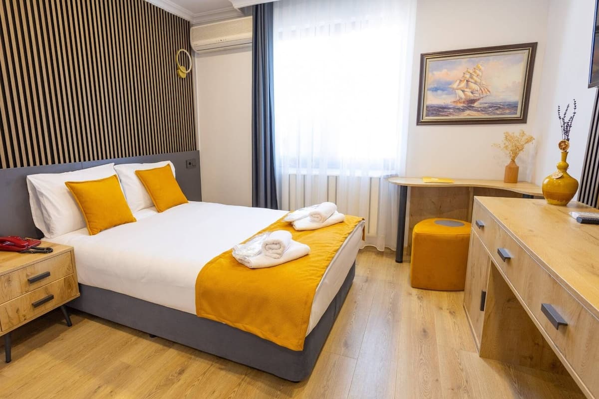 A hotel room with a bed, bedside table, and a desk with a chair.