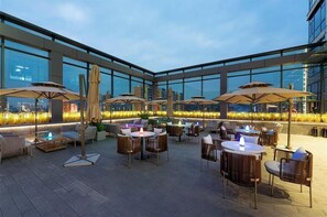 Un bar en la azotea con mesas al aire libre, grandes sombrillas y vistas de la ciudad.