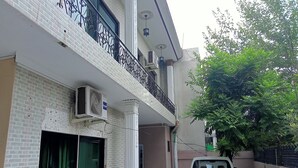 A two-story building with a balcony, air conditioning units, and a tree in the background. - Welcome Inn Guest House (Islamabad)
