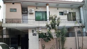 A two-story residential building with a gated entrance, air conditioning units, and a small garden area. - Welcome Inn Guest House (Islamabad)