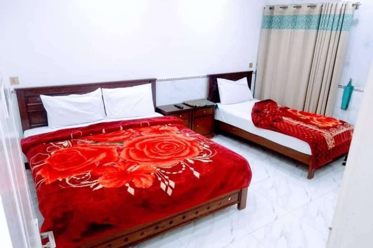 A hotel room with two beds, each with a red floral bedspread.