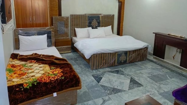 A bedroom with a bed, a wardrobe, a small table, and a decorative headboard. - Welcome Inn Guest House (Islamabad)