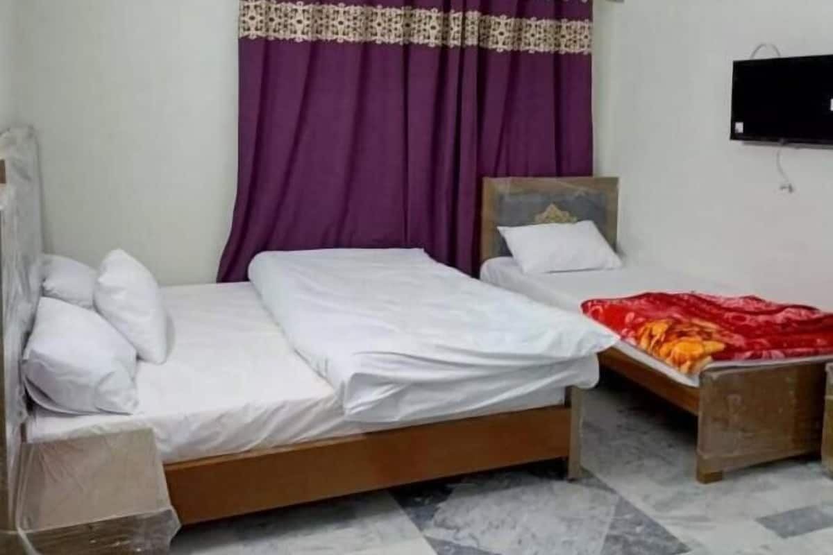 A room with a bed, a small table, a ceiling fan, and a TV mounted on the wall.
