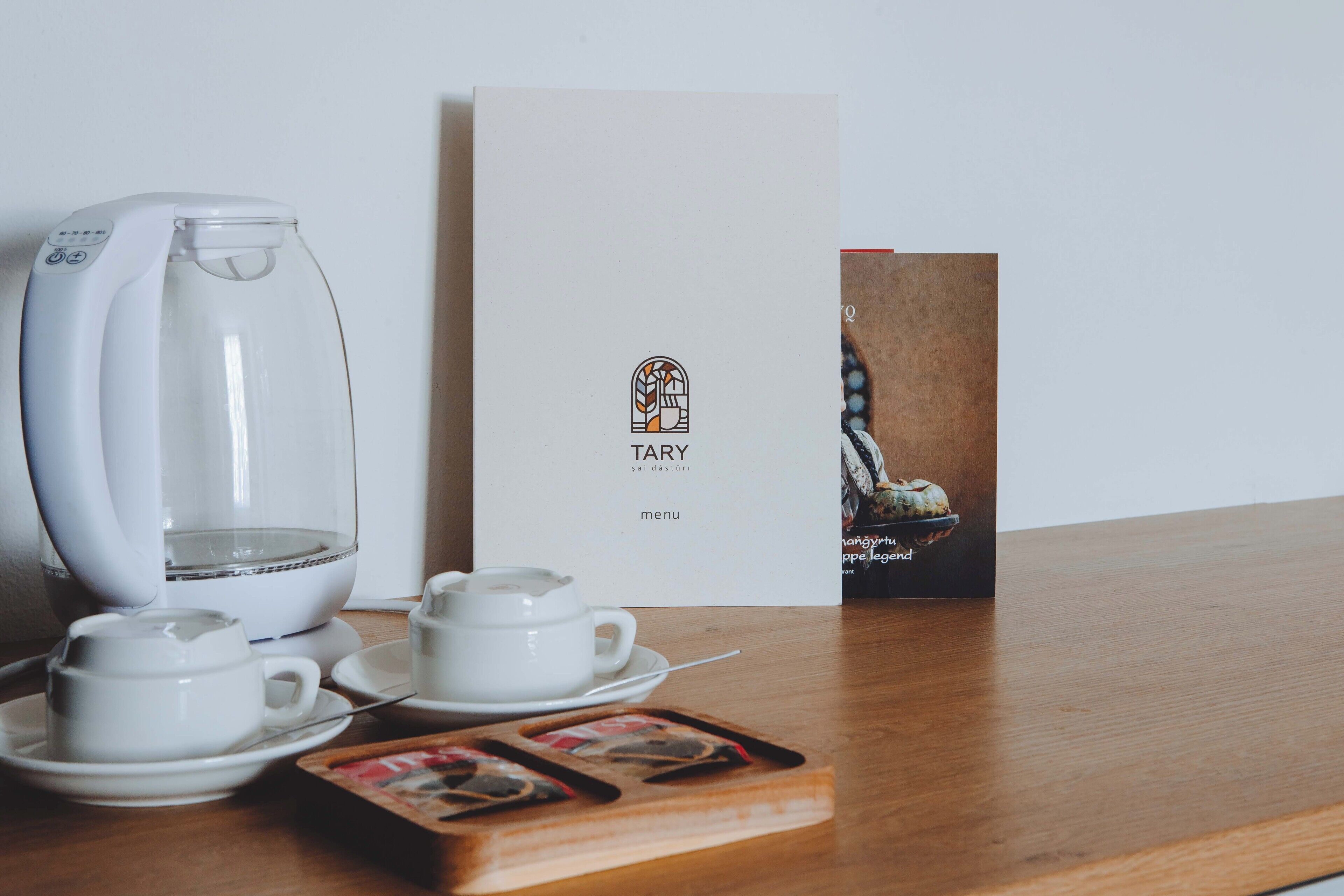 A coffee maker, two cups, a menu, and a tray with coffee capsules on a wooden table.