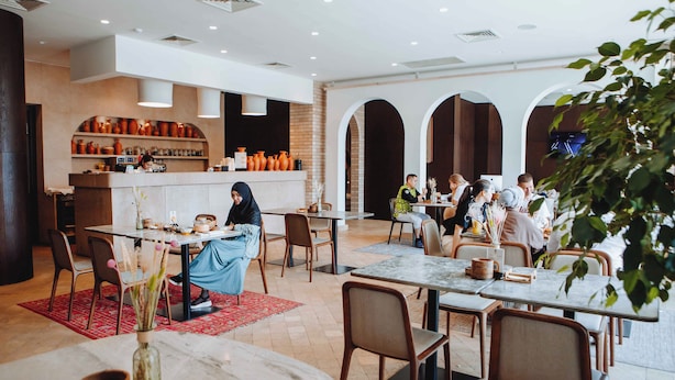 A spacious restaurant with multiple tables and chairs, a bar area with shelves of bottles, and a visible kitchen. - Pana Boutique Hotel (Shymkent)