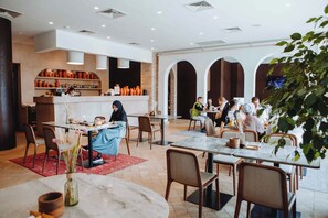 Un restaurant spacieux avec de nombreuses tables et chaises, un bar doté d’étagères remplies de bouteilles et une cuisine ouverte.