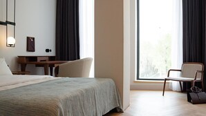A hotel room with a bed, a desk, two chairs, a large window, and a view of greenery outside. - Pana Boutique Hotel (Shymkent)