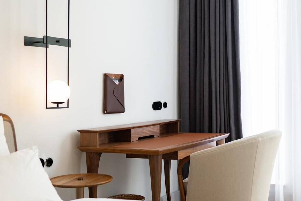 Une chambre d’hôtel équipée d’un lit, d’un bureau, d’une chaise, d’une petite table et d’une lampe fixée au mur.