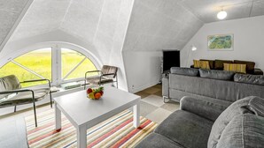 A modern loft bedroom with a sloped ceiling, a large window, a gray sofa, a small table with fruit, and a colorful striped rug. - "Darleen" - 850m to the fjord by Interhome (Vemb)