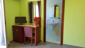 Quarto com escrivaninha, cadeira, computador e um vaso de flores.