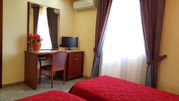 A hotel room with two single beds, a desk with a computer, a chair, a mirror, and a window with curtains.