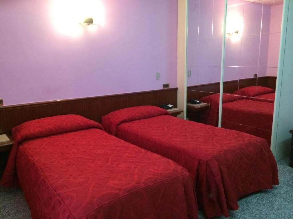 A hotel room with two single beds, a mirror, and a nightstand with a phone.