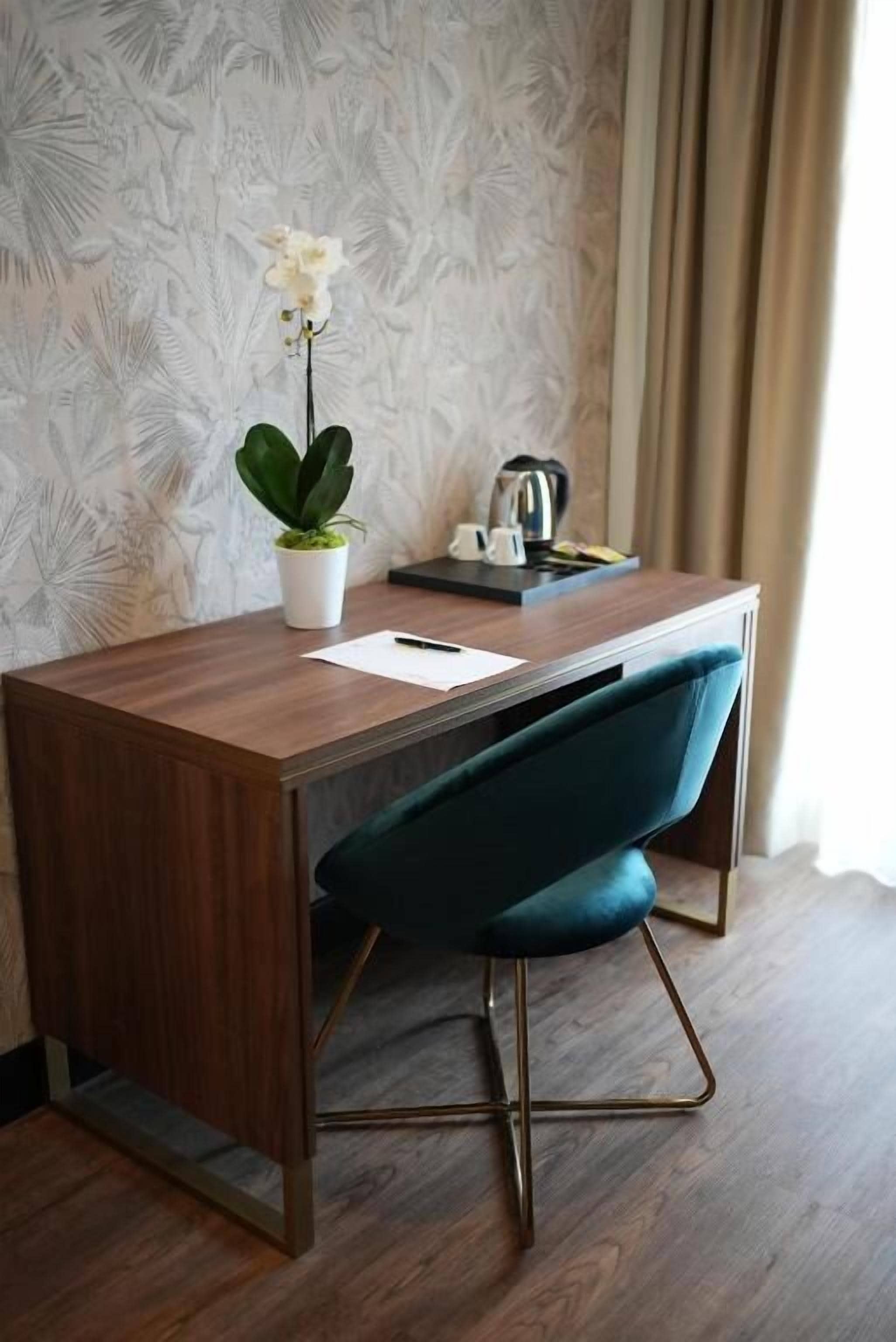 A modern room with a wooden desk, a blue chair, a potted plant, and a kettle.