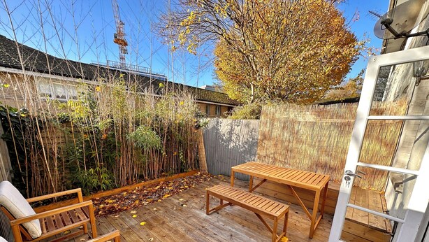 A wooden deck with a table and benches, surrounded by bamboo and a tree. - Charming 1-Bedroom House in Wonderful London with WiFi (London)