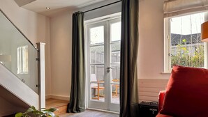 A room with a staircase, a red couch, a black table with a plant, and a view of a wooden deck through a glass door. - Charming 1-Bedroom House in Wonderful London with WiFi (London)