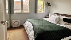 A bedroom with a bed, two windows, a radiator, and a hanging plant. - Charming 1-Bedroom House in Wonderful London with WiFi (London)
