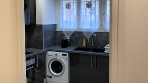 Eine kleine Küche mit integriertem Waschmaschinenanschluss, Spüle und einem Fenster mit Dekorationselementen.