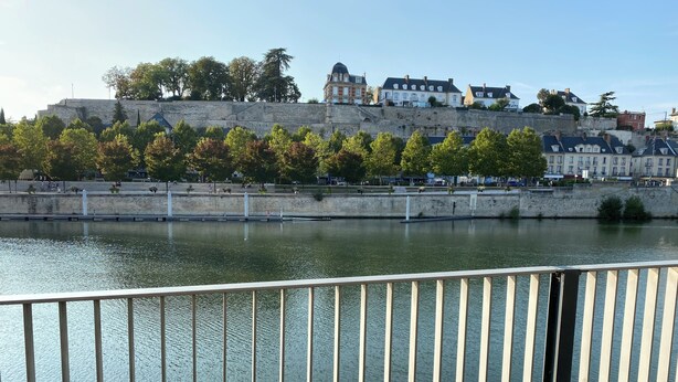 Ein Fluss mit einer Steinmauer und Gebäuden am gegenüberliegenden Ufer.