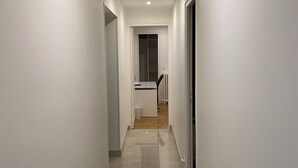 Ein Flur mit weißen Wänden, gefliestem Boden und einer eingelassenen Deckenleuchte.
